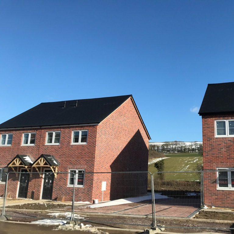 Newly constructed modern homes with gray Envirotile roofing, showcasing a uniform, eco-friendly tile pattern under clear blue skies at a residential development site. Newly constructed modern homes with gray Envirotile roofing, showcasing a uniform, eco-friendly tile at a residential development site